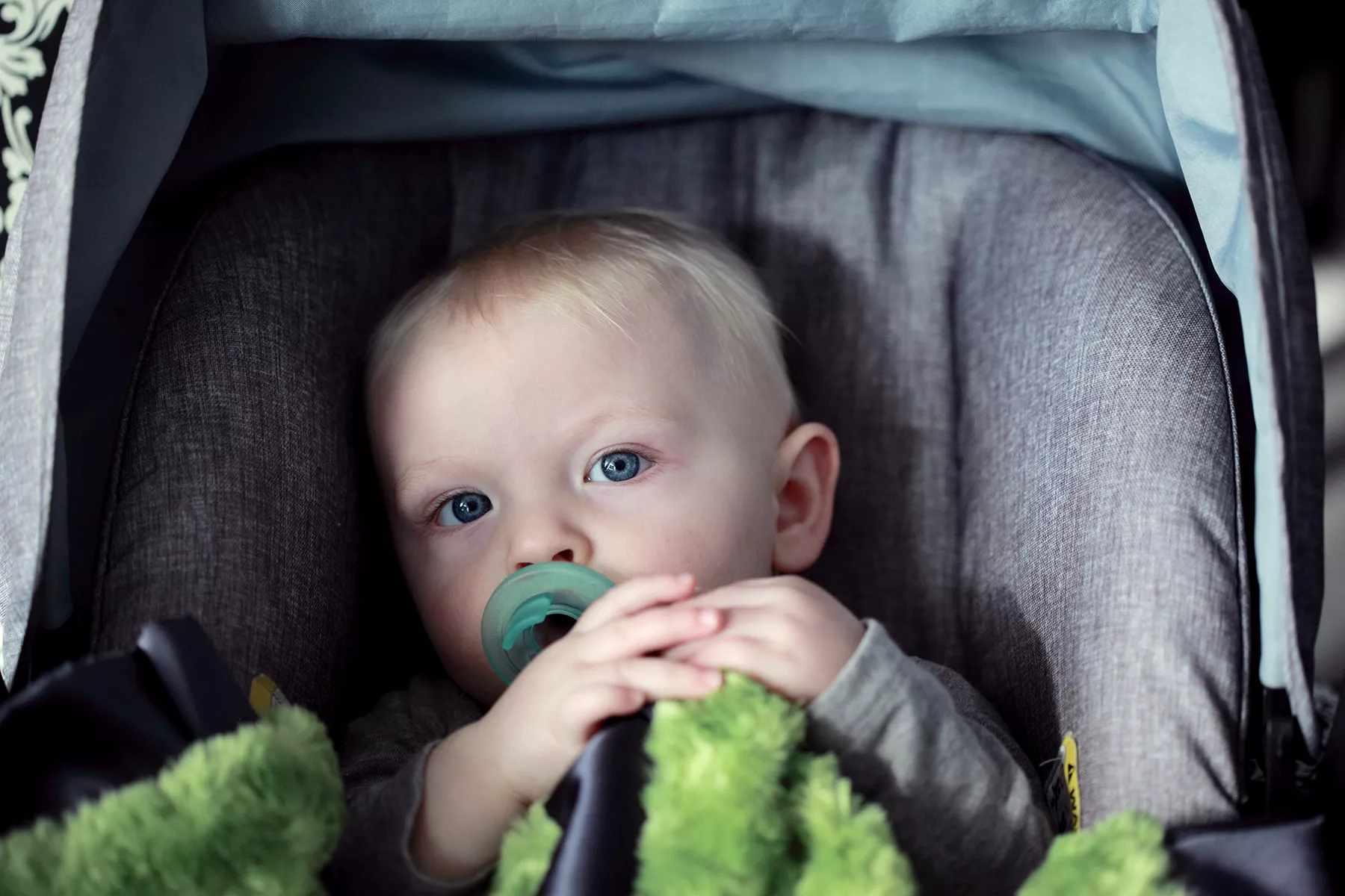 Ein Kleinkind mit Kuscheltier und Schnuller in einem Kindersitz