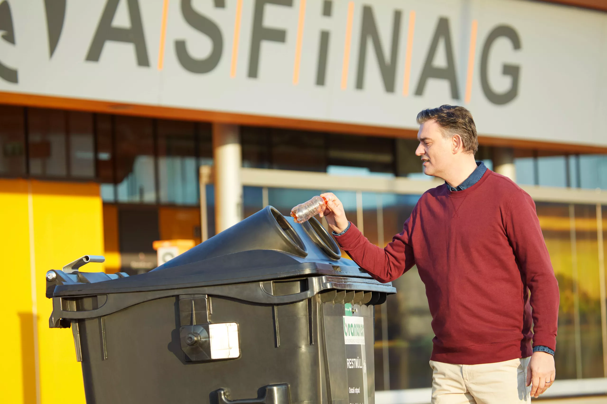 Ein Mann wirft vor einem ASFINAG Rastplatz eine Plastikflasche in eine Mülltonne