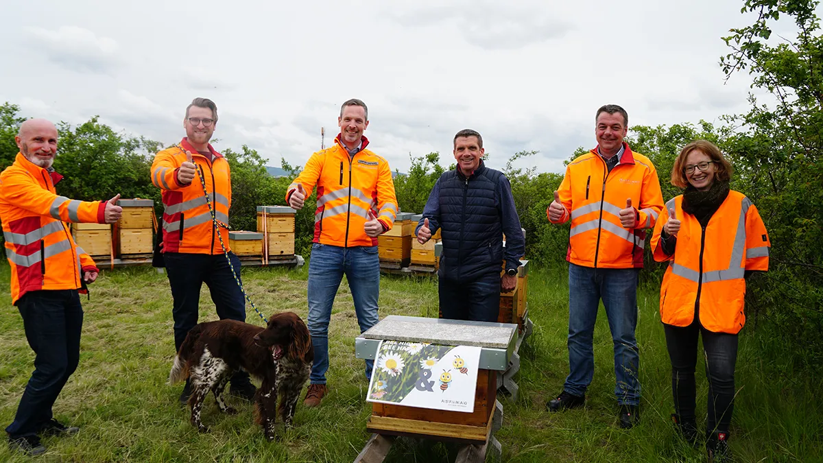 Das ASFINAG Bienen Team stehen gemeinsam mit einem Jagdhund vor Bienenstöcken