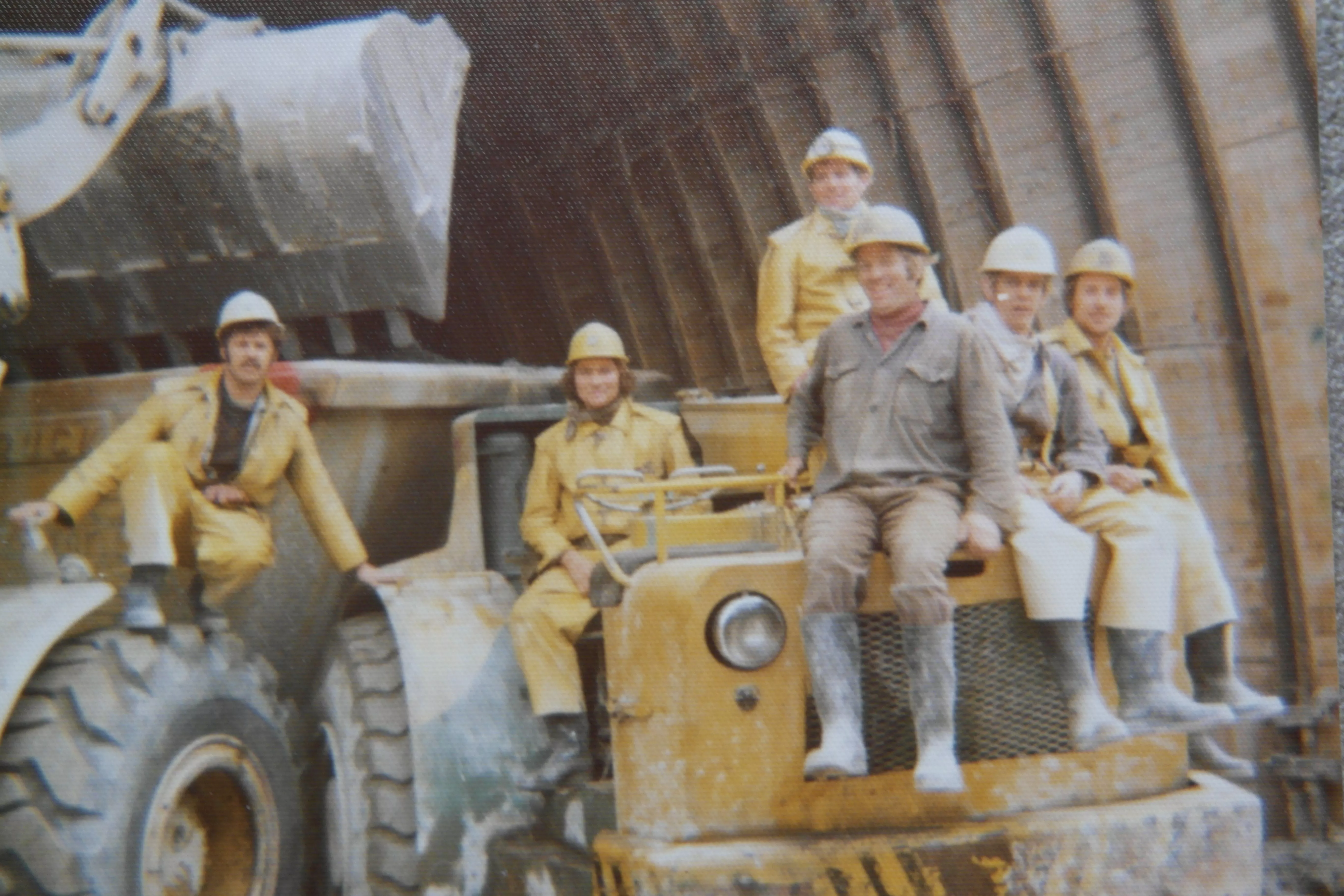 Sechs Menschen in Arbeitskleidung sitzen auf einem gelben Baustellenfahrzeug