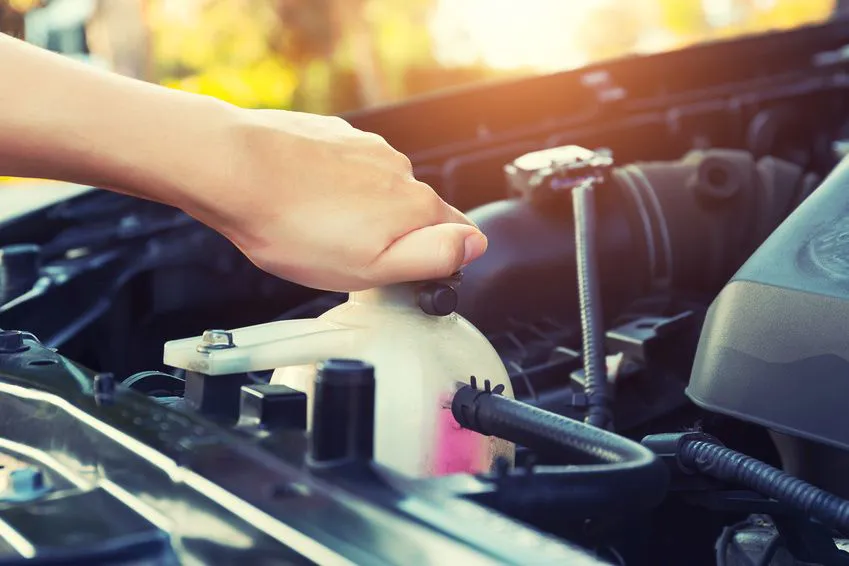 Eine Hand greift in den Motorraum eines Autos