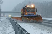 Schneepflug mit ausgeklapptem Seitenflügel auf verschneiter Autobahn
