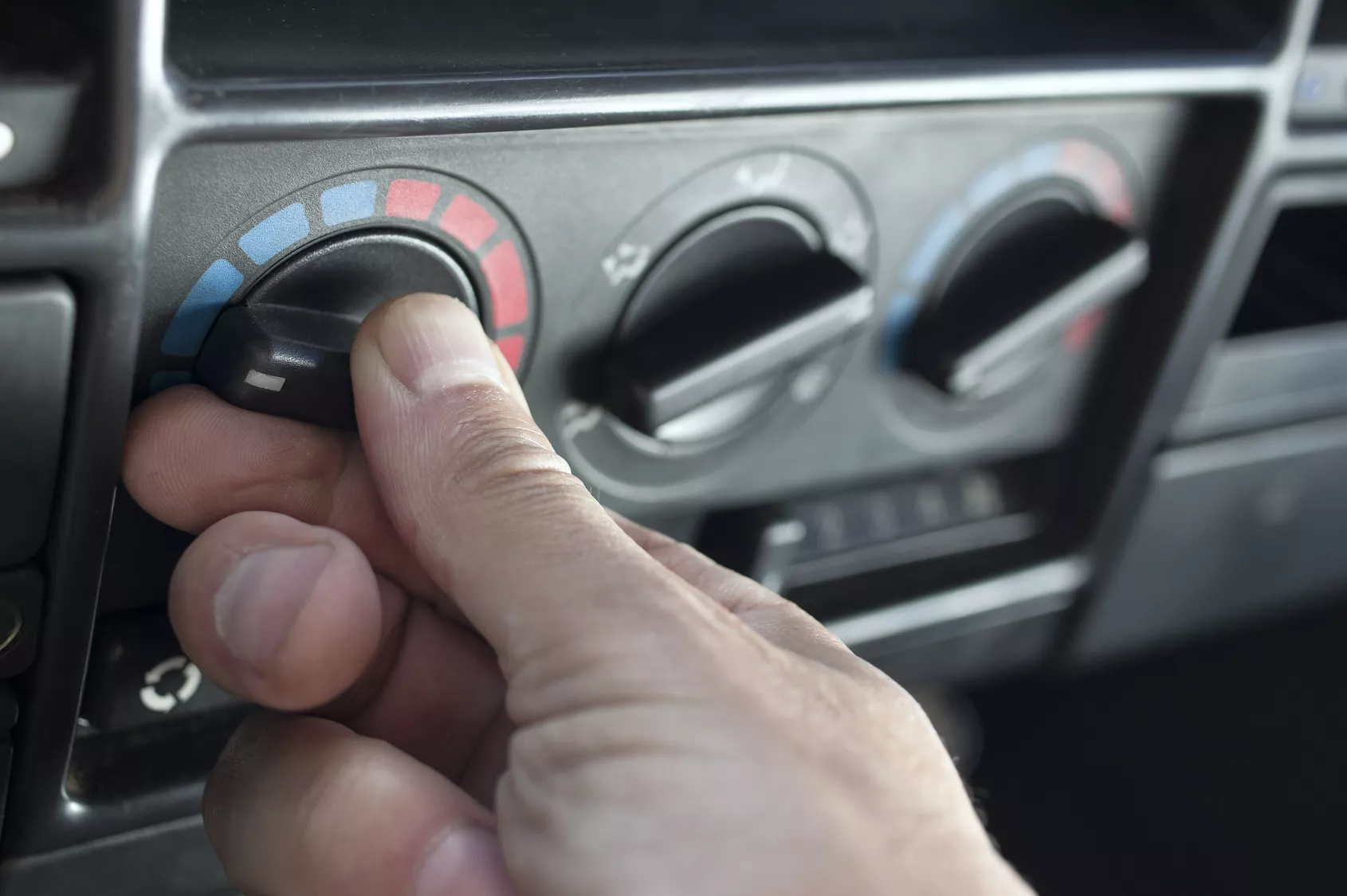 Eine Hand dreht an einer Klimaanlage im Auto