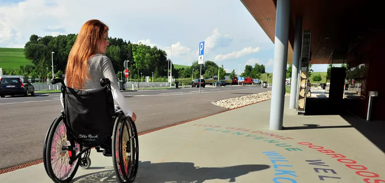 Junge Frau im Rollstuhl vor einem ASFINAG Rastplatz