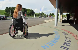 Junge Frau im Rollstuhl vor einem ASFINAG Rastplatz