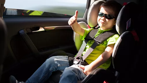 Ein Kind im Kindersitz mit Sonnenbrille zeigt einen Daumen hoch