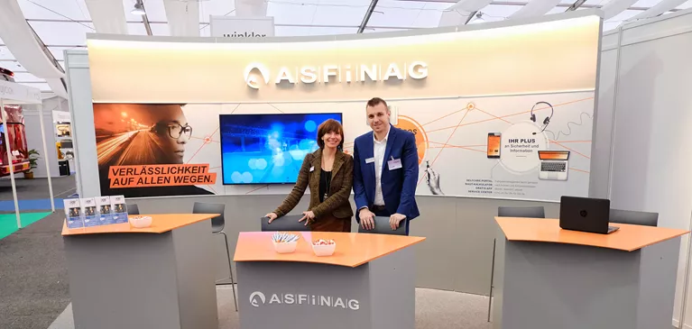 Eine Frau und ein Mann stehen hinter einem Tisch des ASFINAG Stands bei der Businessmesse Prag