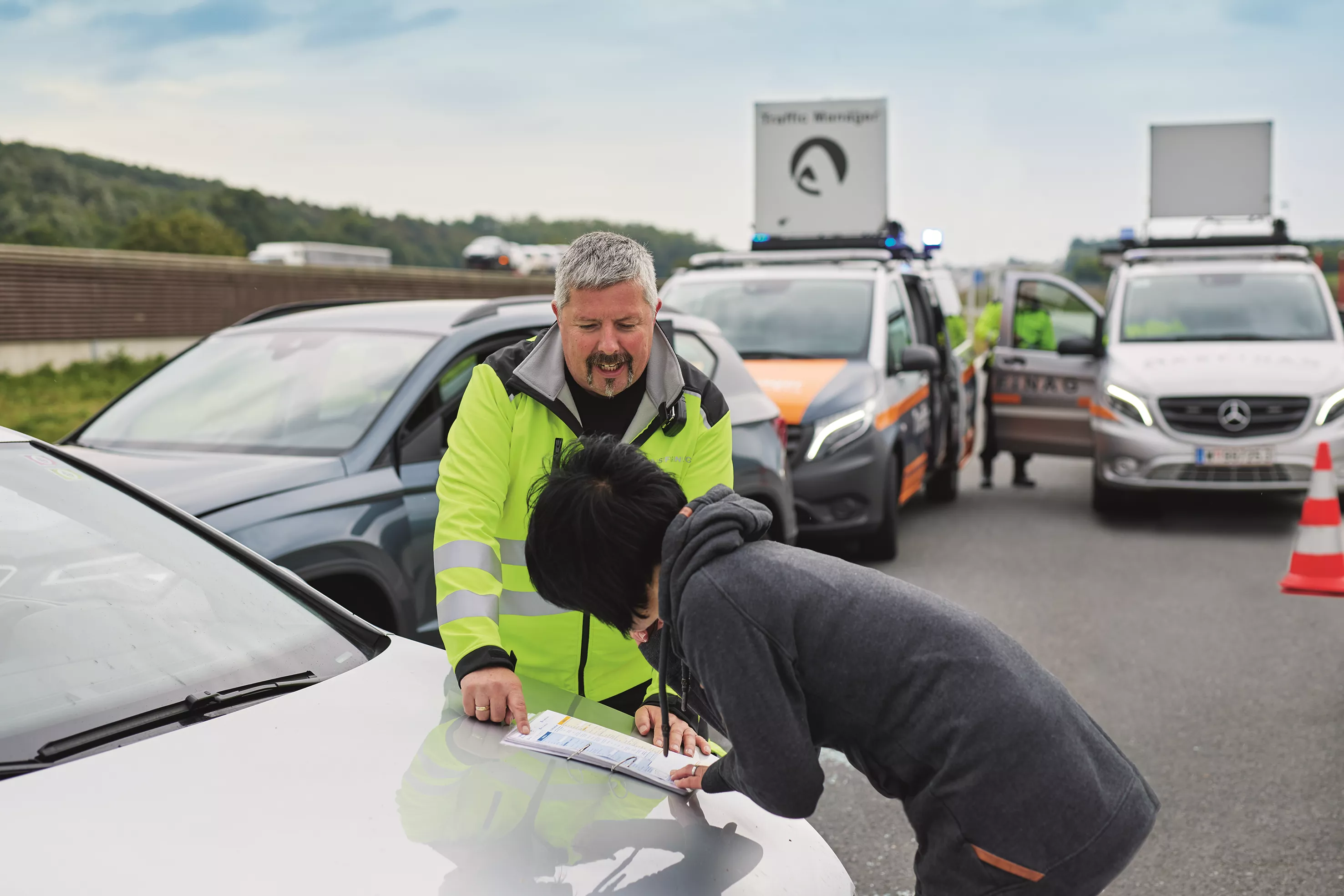 Ein ASFINAG Traffic Manager hilft einer Frau beim Ausfüllen eines Unfallberichts auf der Motorhaube
