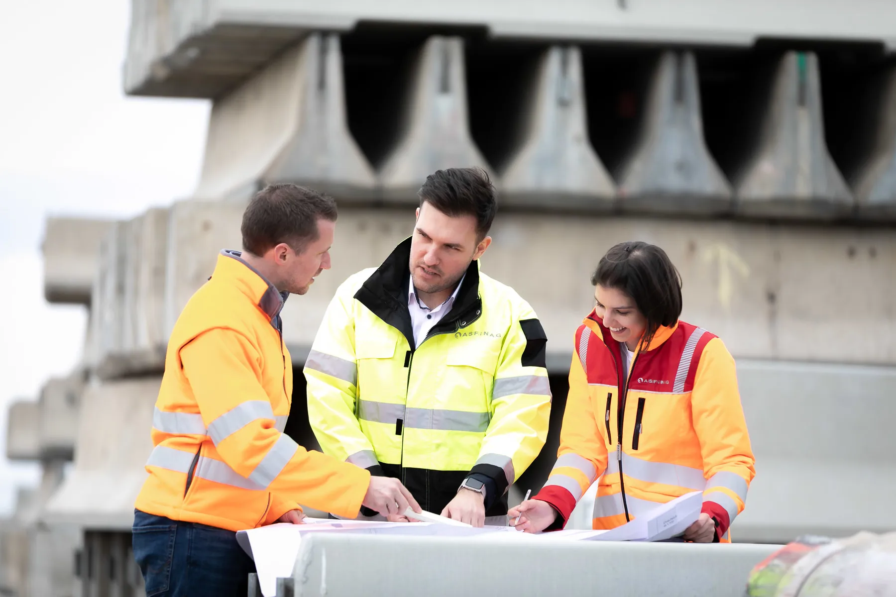 Eine Frau und zwei Männer mit Warnwesten auf einer Baustelle