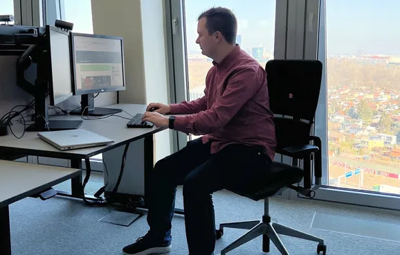 Ein junger Mann sitzt an einem Schreibtisch vor einem Computer und lächelt in die Kamera