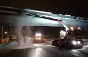 Lkw mit Kran bürstet Schnee von einer Brücke bei Nacht