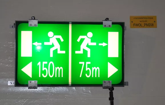 Grün/weiße Hinweistafeln zeigen die Distanz zum Fluchtweg an