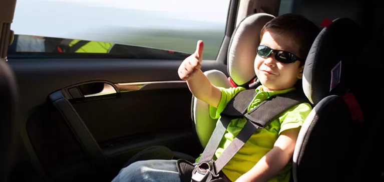 Ein Kind im Kindersitz mit Sonnenbrille zeigt einen Daumen hoch