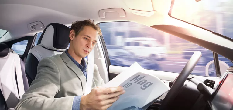 Fahrer liest Zeitung, während er im hinterm Lenkrad sitzt und das Auto selbständig fährt